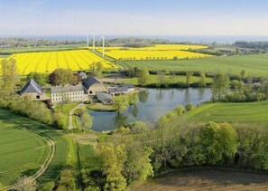Ländliche Landschaft mit einem großen Gebäudekomplex, einem See und Feldern mit gelbem Getreide.