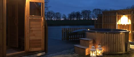 A wooden hot tub with lanterns, a wooden deck, and a wooden building with a door.