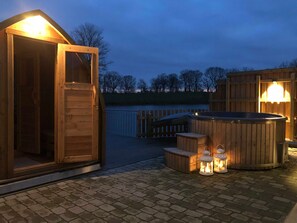 Ein hölzernes Whirlpool mit Laternen, eine Holzterrasse und ein Holzgebäude mit einer Tür.