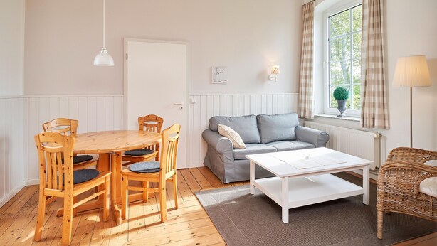 Ett mysigt vardagsrum med ett matbord i trä, en grå soffa och en fåtölj i rotting.