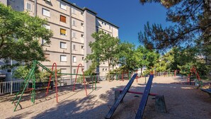 Ein Spielplatz im Freien mit Schaukeln und Klettergerüsten, umgeben von Bäumen und einem Gebäude im Hintergrund.