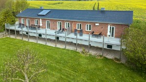 A brick house with a balcony overlooking a field of yellow flowers. - Remise I - Holiday apartments Gut Oestergaard (Steinberg)