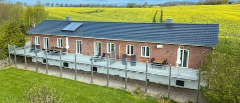 A brick house with a balcony overlooking a field of yellow flowers.