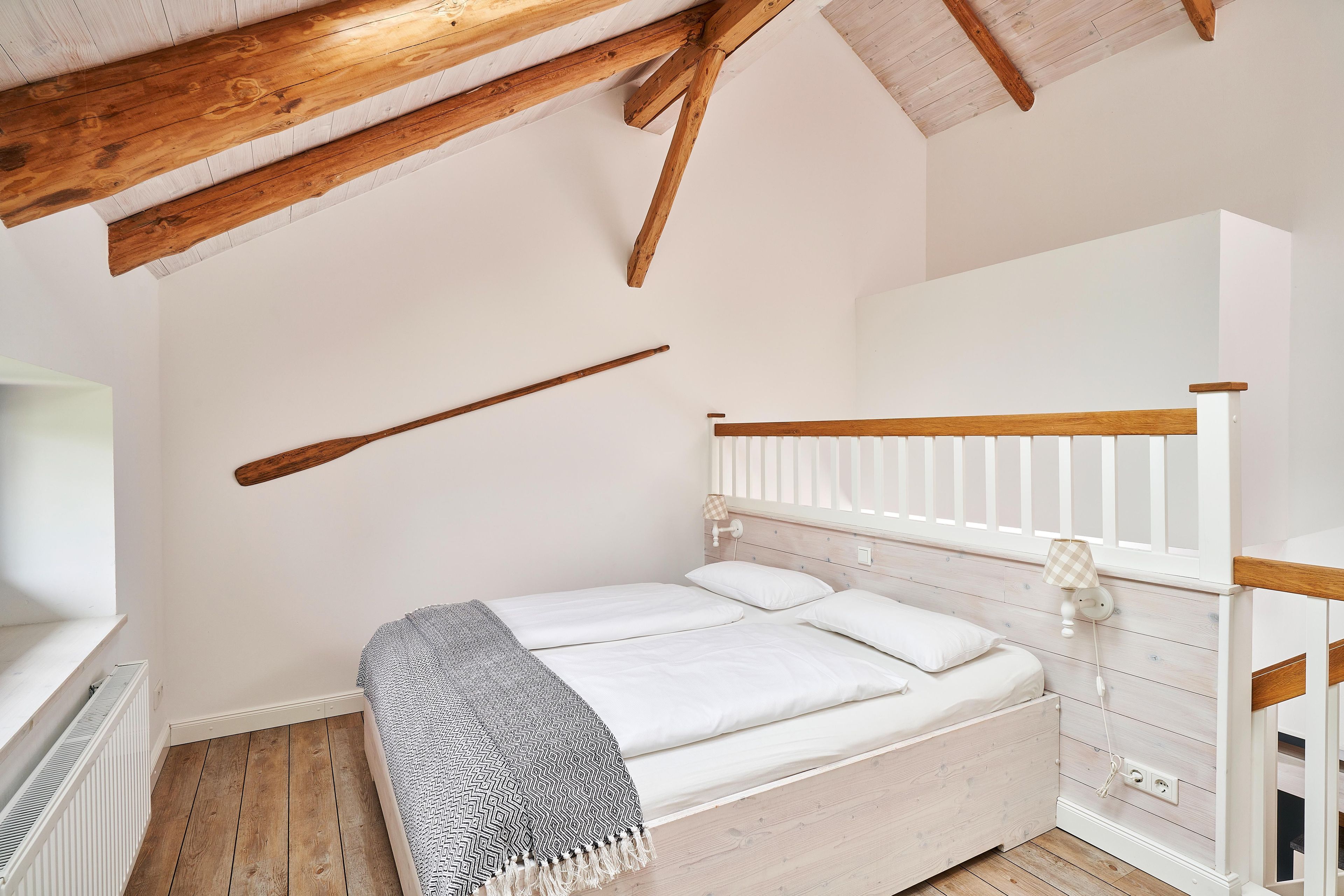 Ein Schlafzimmer mit Holzboden, weißen Wänden, einem Bett mit weißer Bettwäsche und einem Fenster mit weißem Heizkörper.