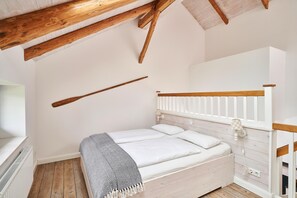 Une chambre avec un plafond en bois, des murs blancs, un lit avec une literie blanche et une fenêtre avec un radiateur blanc.
