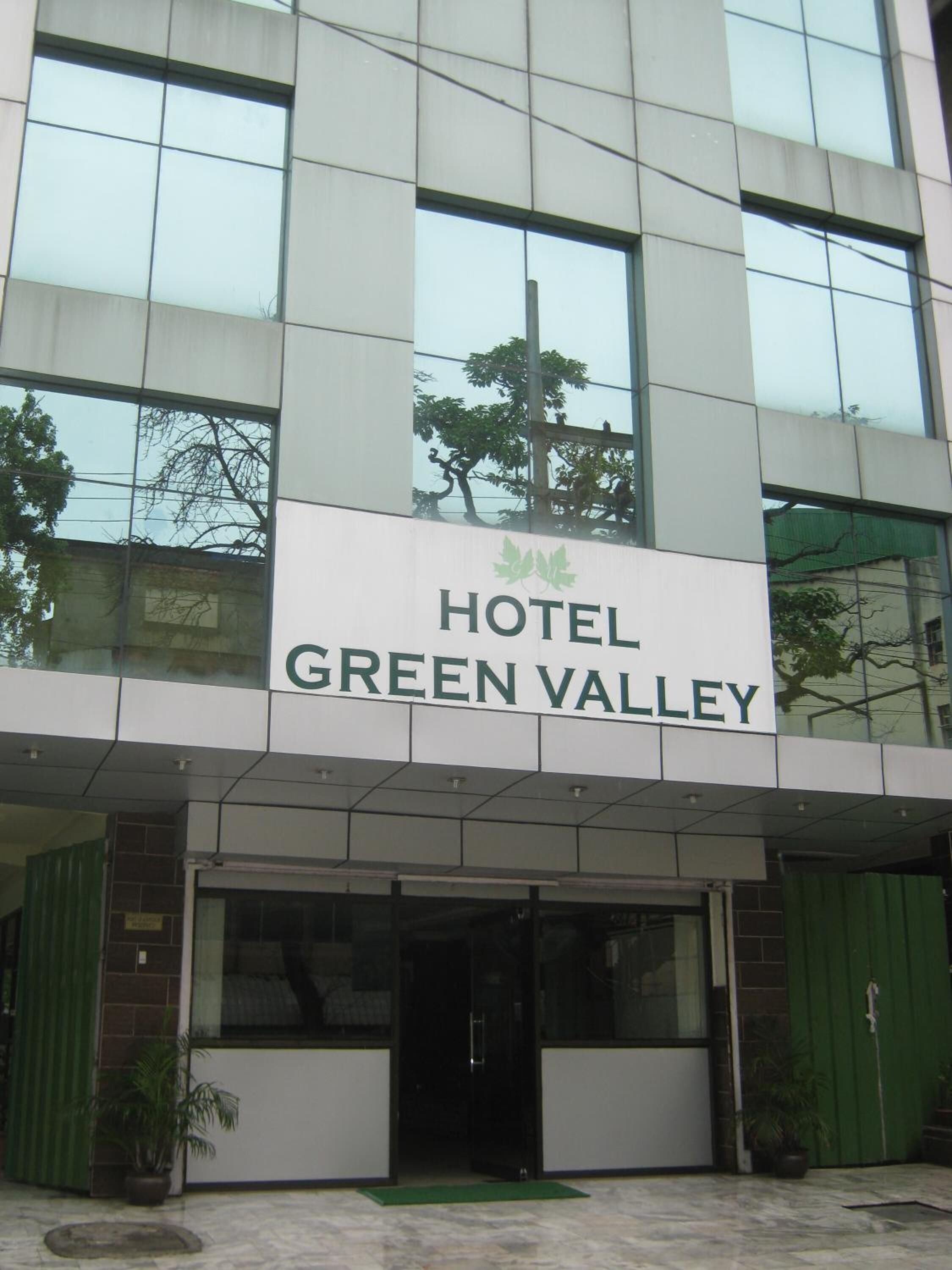 A modern hotel building with a sign reading "HOTEL GREEN VALLEY".