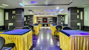 Un salón de conferencias con mesas cubiertas con manteles amarillos, dispuestas en filas frente a un escenario central con una pantalla de televisión.