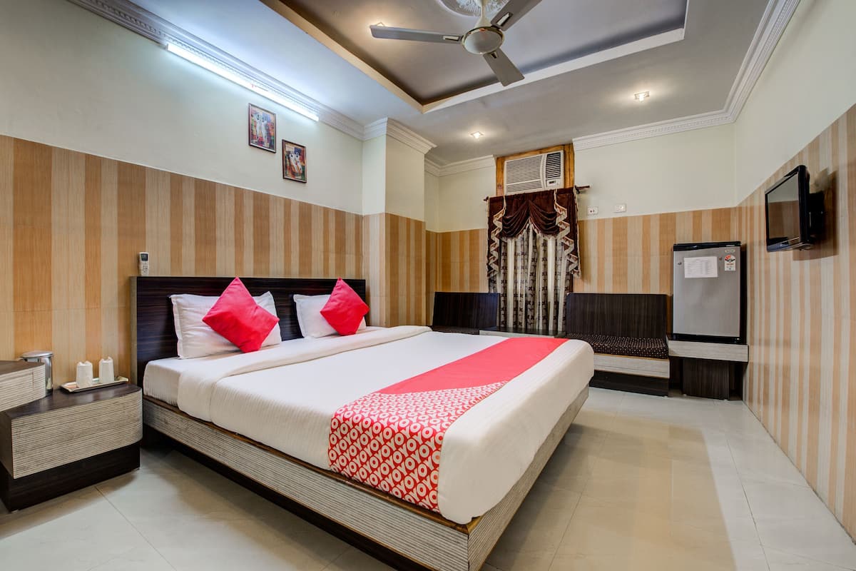 A hotel room with a large bed, a bedside table, a nightstand, a ceiling fan, a TV, and a window with curtains.
