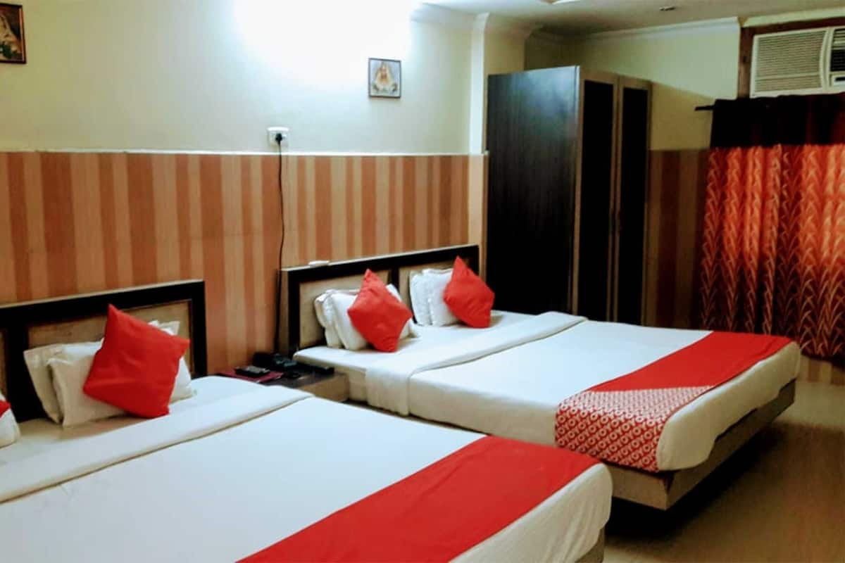 A hotel room with two beds, each with red pillows and a red and white bedspread. There is a wardrobe and a window with curtains.