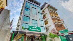 Un hotel llamado "Hotel Green Valley" con una fachada moderna, amplias ventanas y una entrada verde.