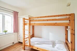 Ein Stockbett mit Holzrahmen, weißer Bettwäsche und einem Fenster mit Vorhang.