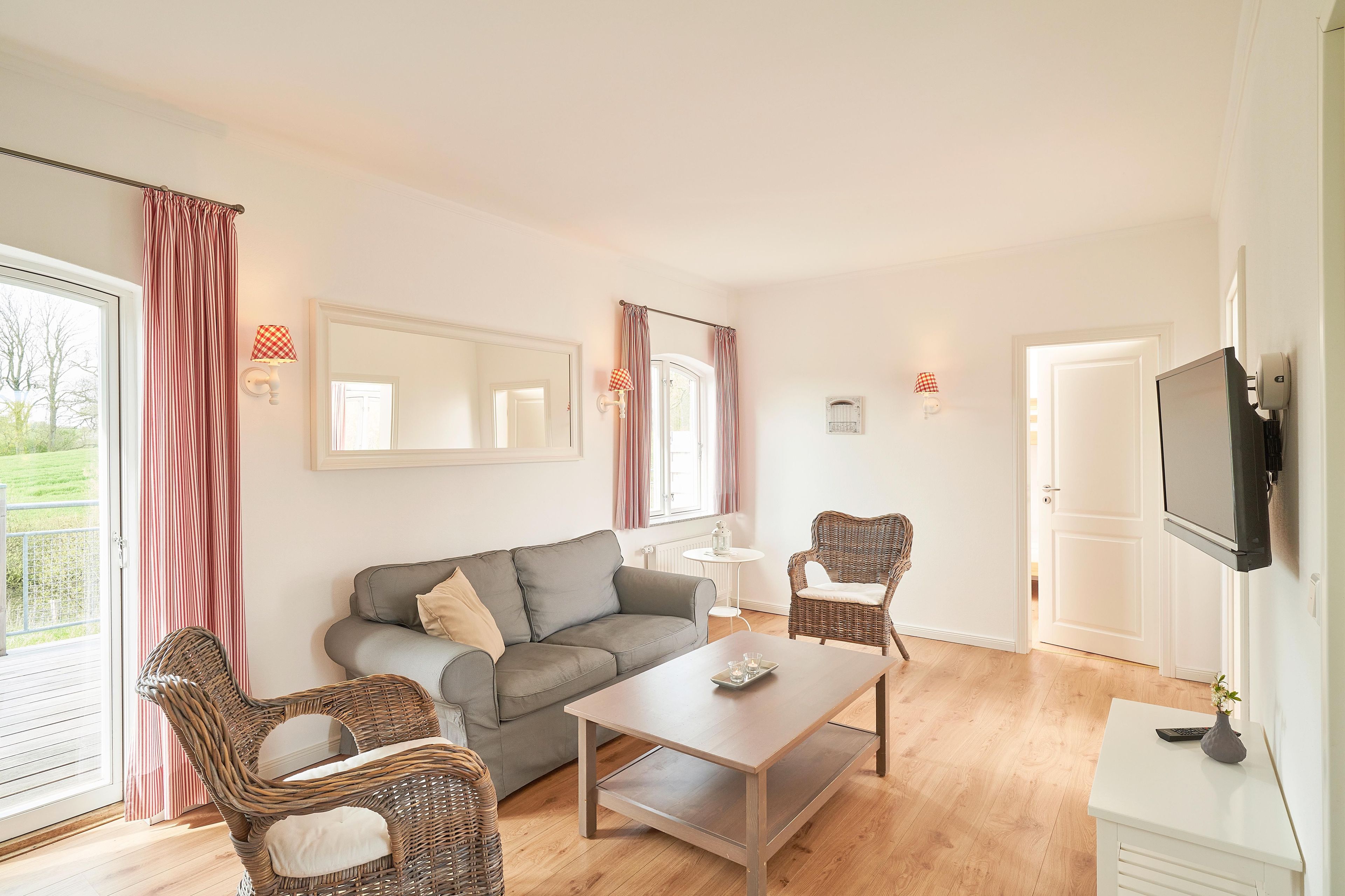 Un salon avec un canapé gris, deux fauteuils en osier, une table basse en bois et un téléviseur à écran plat fixé au mur.