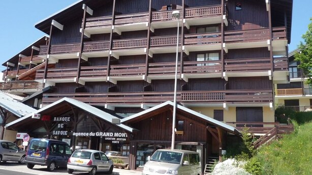 En bygning med flere etager, balkoner, et skilt med 'Banque de Savoie' og flere parkerede biler.