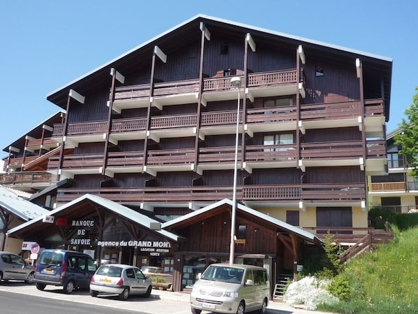 A multi-story building with balconies, a sign for 'Banque de Savoie', and several parked cars.