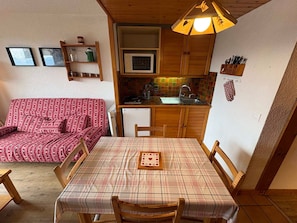 A compact living space with a kitchenette, a dining table with chairs, a sofa, and a ceiling light fixture.