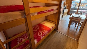 En køjeseng med rødt og hvidt sengetøj, trævægge og udsigt til et spiseområde med et bord og stole.