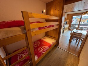 A bunk bed with red and white bedding, wooden walls, and a view of a dining area with a table and chairs. - Sunny studio for 4, view on the slopes (Les Saisies)
