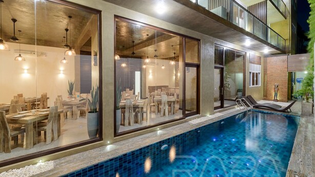 A modern indoor pool area with a glass wall, wooden furniture, and ceiling lights. - Hotel Sico (Negombo)