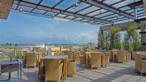 An outdoor patio with wicker furniture and a glass ceiling, overlooking a coastal view. - Hotel Sico (Negombo)
