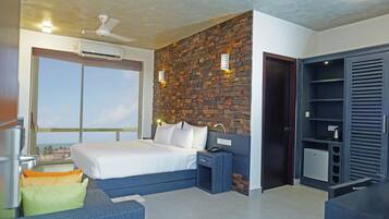 A bedroom with a large bed, a brick accent wall, a wardrobe, and a view of the ocean.