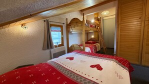 Une chambre mansardée chaleureuse, avec un lit superposé, une fenêtre avec des rideaux et une armoire en bois.