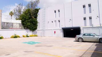 Un estacionamiento con un coche, un edificio con garaje y un árbol.