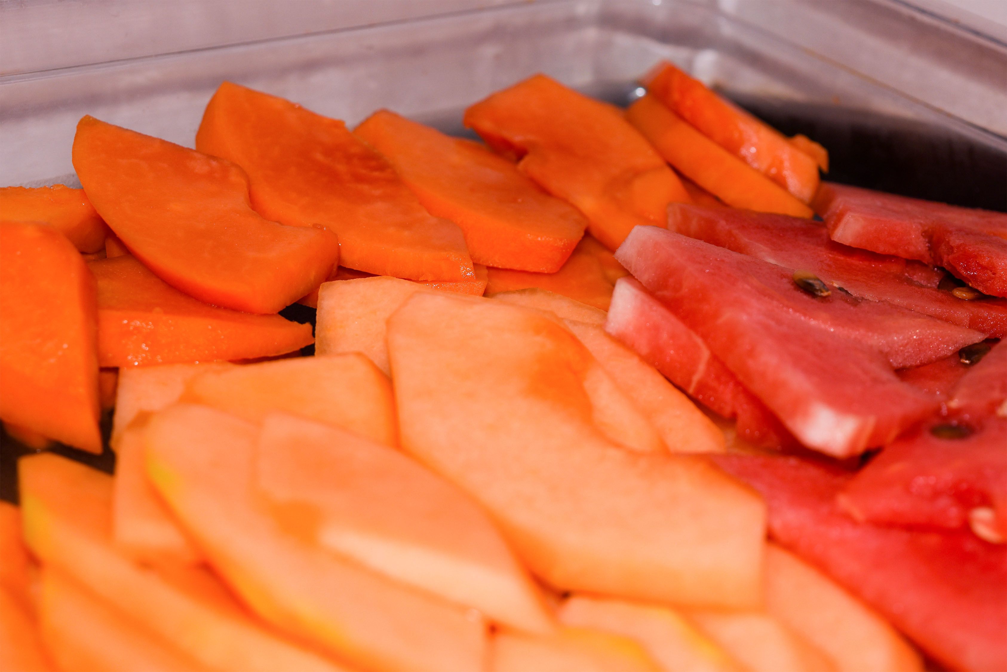 A container with sliced fruits including cantaloupe and watermelon.