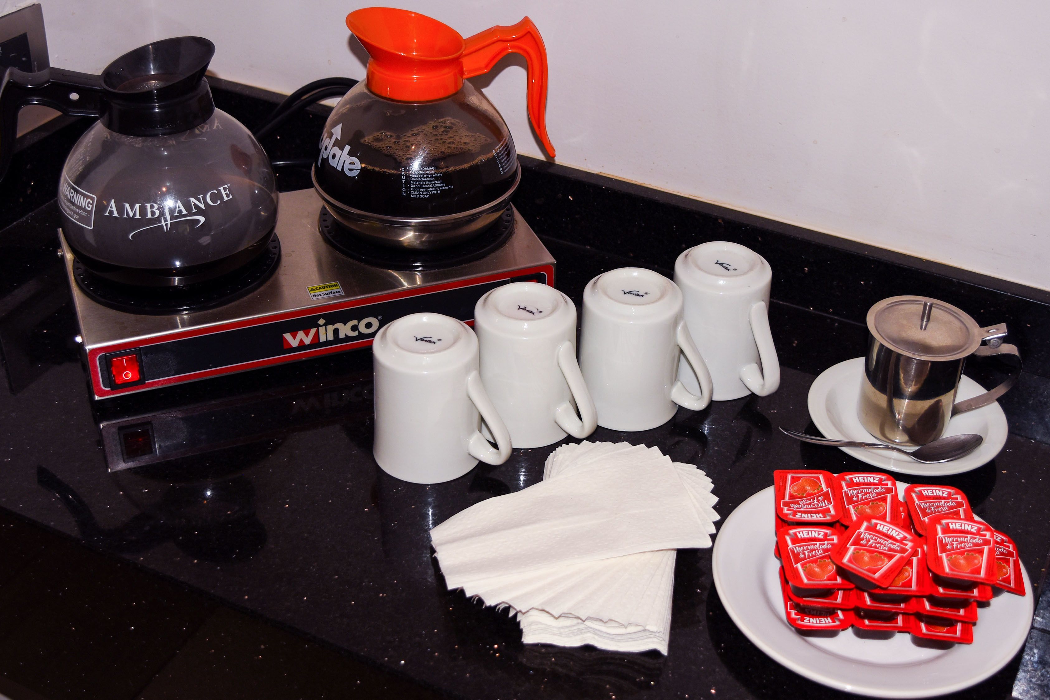 Eine Küchenarbeitsplatte mit Kaffeemaschine, Wasserkocher, weißen Tassen, einer Servierplatte mit Gewürzen und einem Löffel.