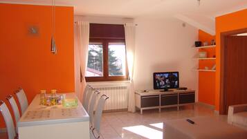 Ein modernes Wohnzimmer mit Essbereich, einem Fernseher und einem fenster mit Vorhängen.