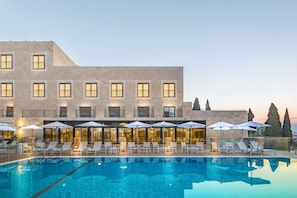 A swimming pool with lounge chairs and umbrellas, a building with multiple windows and balconies, and a clear sky.