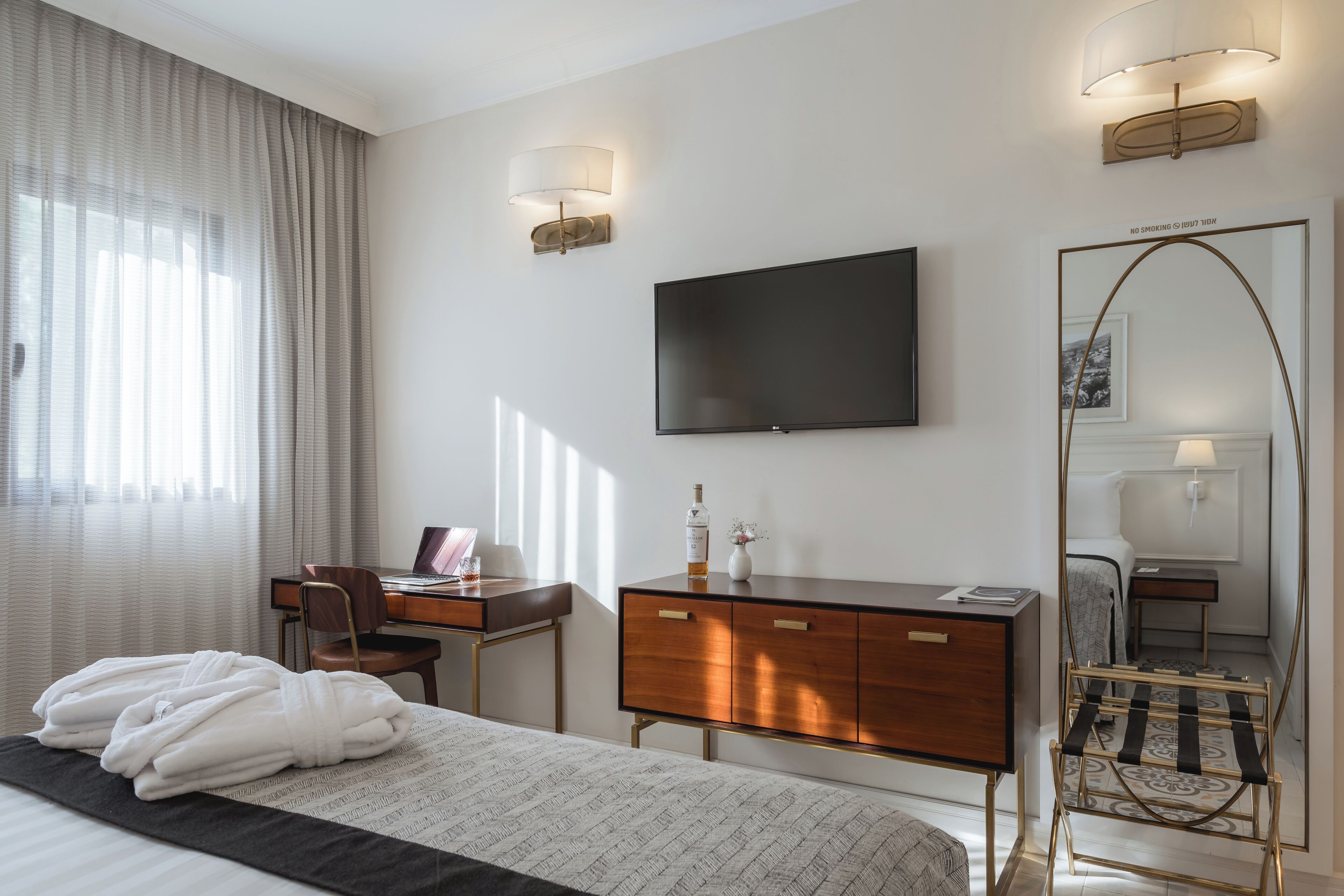 A hotel room with a bed, a desk, a dresser, a TV, and a large mirror.