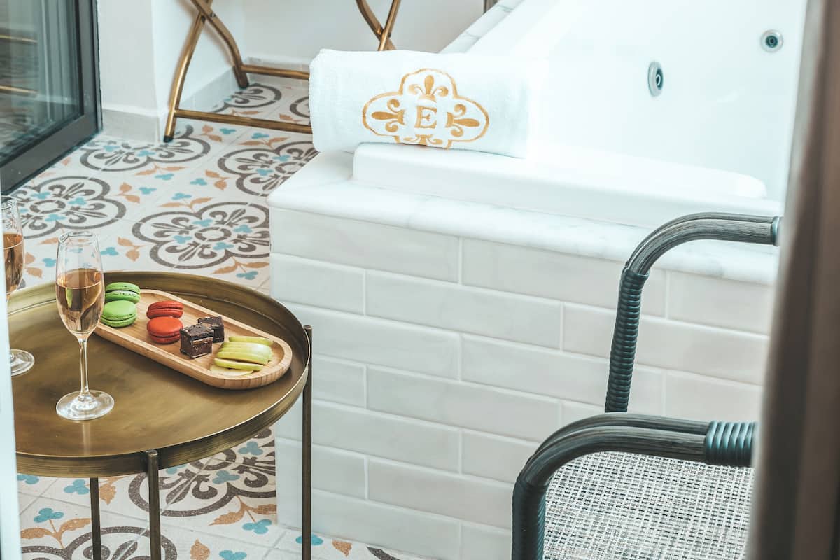 Une salle de bain avec une baignoire, un porte-serviettes, un plateau avec des en-cas et une bouteille de champagne.