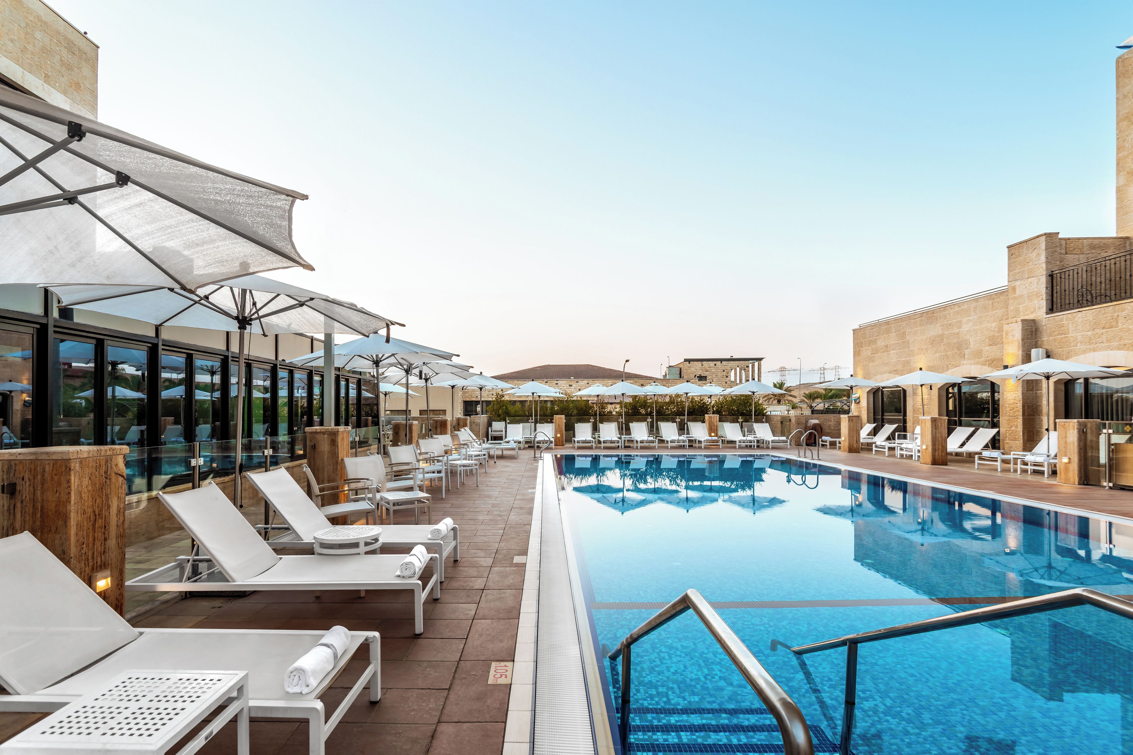 A poolside area with sun loungers and umbrellas, a clear pool, and a view of a mountain in the background.