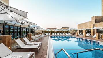 A poolside area with sun loungers and umbrellas, a clear pool, and a view of a mountain in the background.