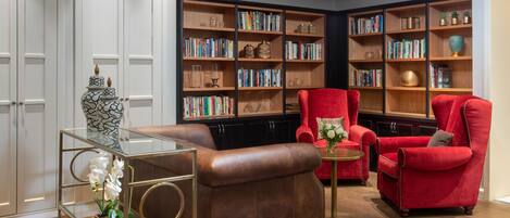 A modern library with leather armchairs, a glass coffee table, and wooden bookshelves filled with books and decorative items.