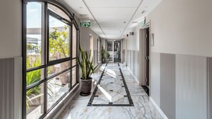 A corridor with large windows, potted plants, and a marble floor. - Edmond Luxury Hotel & Spa (Rosh Pinna)