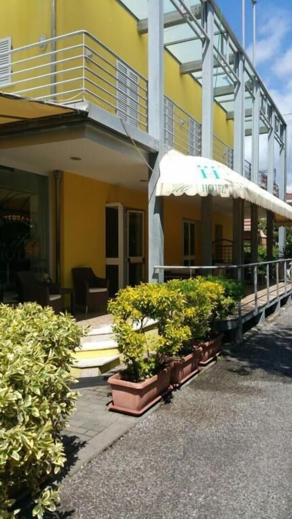 Un hotel con fachada amarilla, área de estar al aire libre y plantas en macetas.