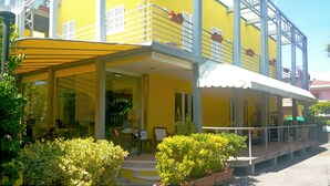 A yellow building with a balcony, a covered entrance, and potted plants. - Hotel Illi  (Massa)
