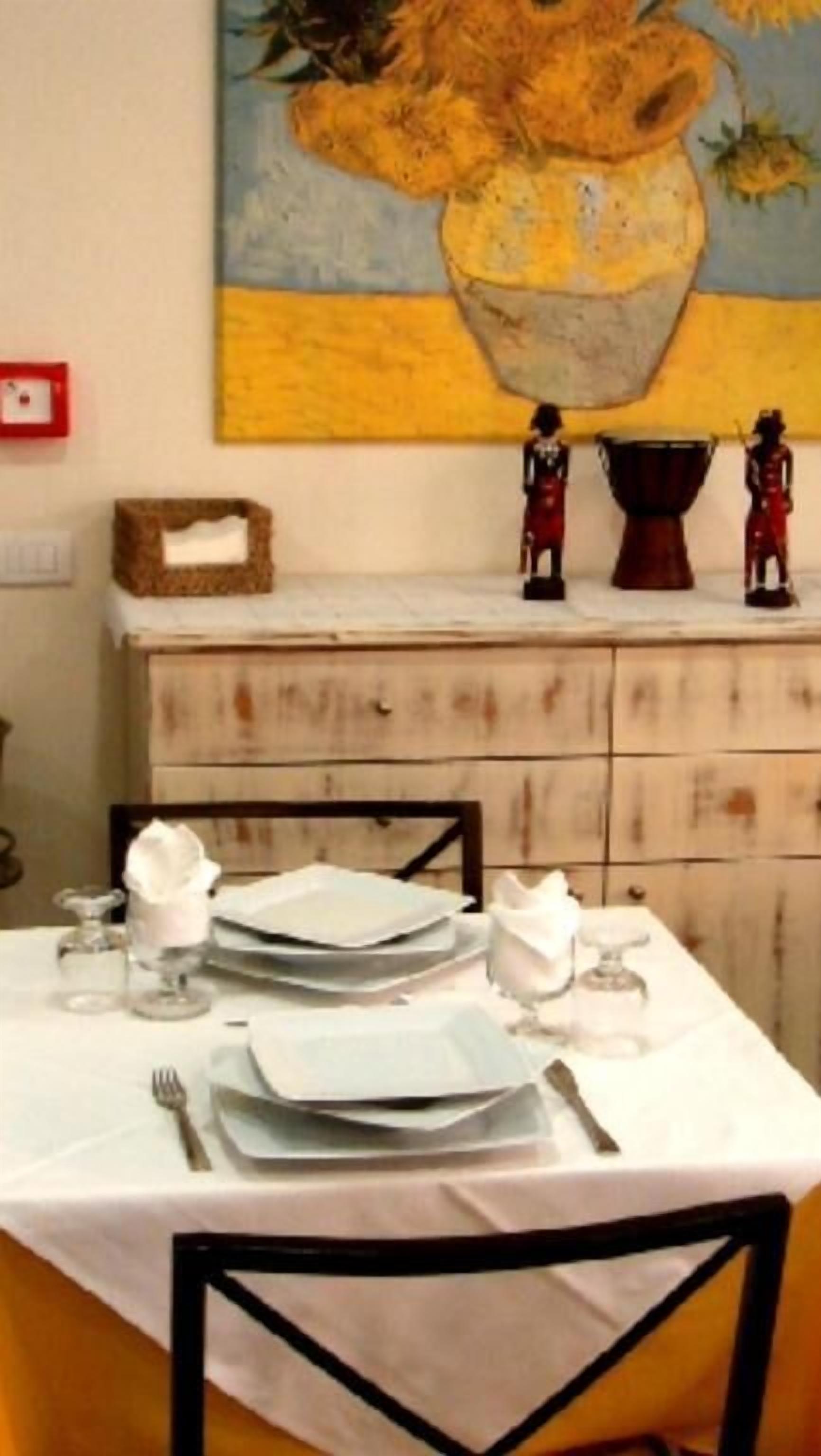 A dining table set with plates, cutlery, and glasses, with a painting and figurines on the wall behind.