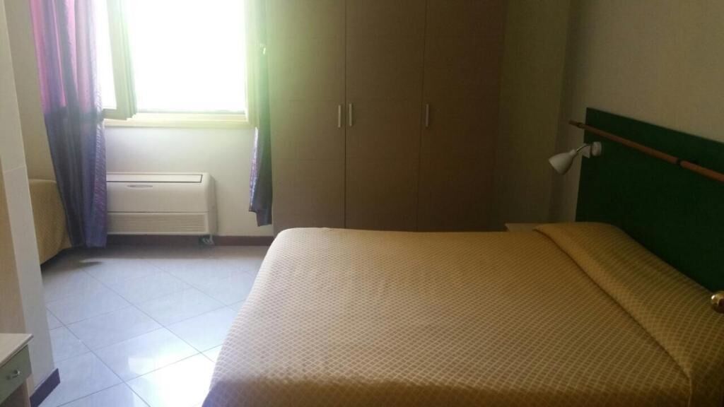 A bedroom with a bed, a wardrobe, a radiator, and a window with curtains.