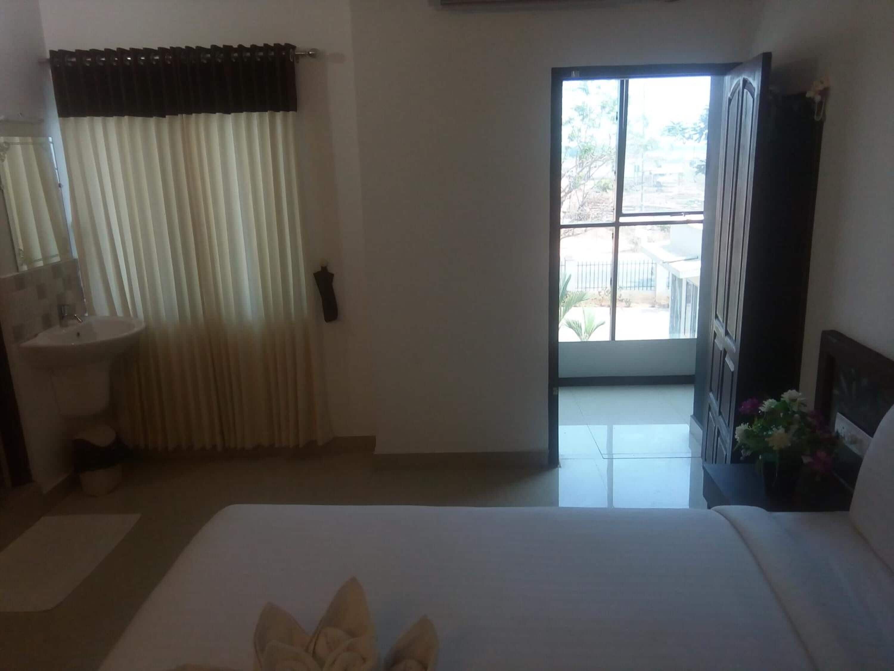 Una habitación de hotel con una cama, una ventana, una puerta, un lavamanos y un espejo.