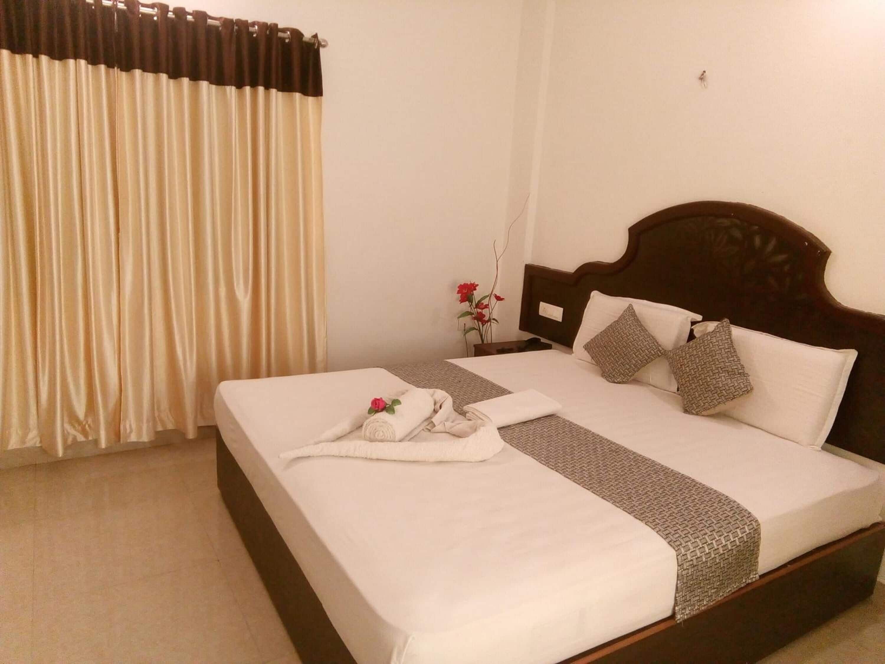 A neatly made bed with a white comforter, two pillows, and a decorative towel with a rose.