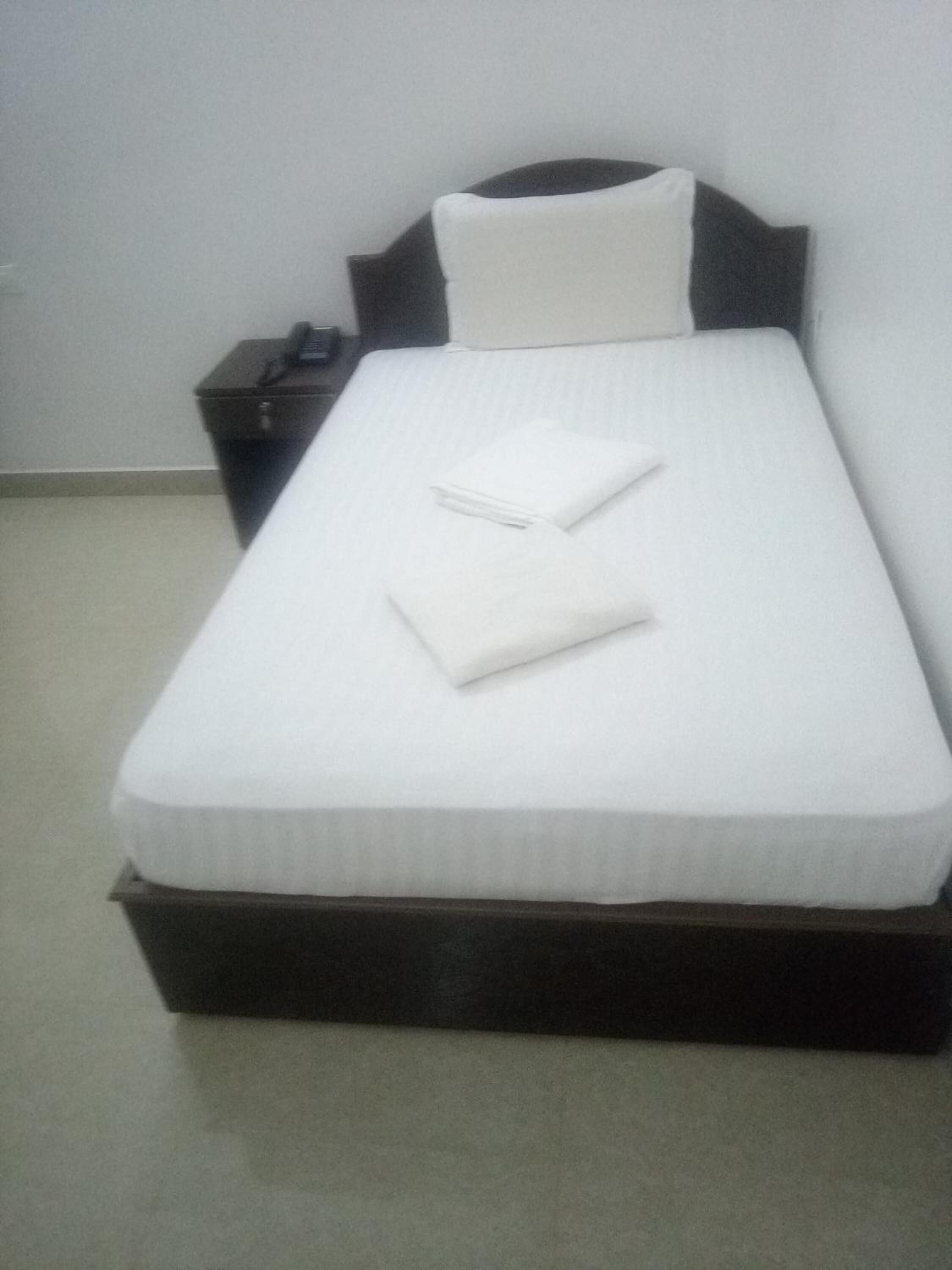 Una cama bien hecha con sábanas y almohadas blancas, un cabecero de madera oscura y una mesita de noche con un teléfono y una lámpara.