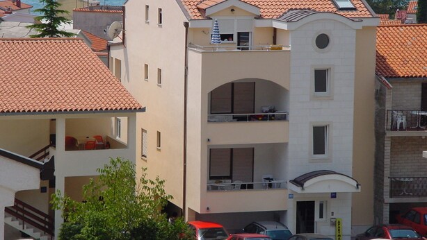 Un edificio de varios pisos con techo de tejas, balcones y vista al mar.