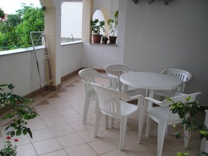 Un pequeño patio con una mesa redonda y cuatro sillas, rodeado de macetas con plantas y un tendedero de metal.