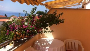 Un balcón con mesa y sillas, vista al mar y una planta con flores.
