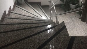Una escalera de granito con barandillas metálicas, que conduce a un rellano con una planta en maceta.