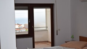 Un dormitorio con cama, una mesita de noche, una lámpara verde y vista al mar a través de una puerta abierta.