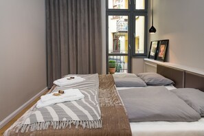 A bedroom with two beds, a window with a view of a balcony, and a small potted plant. - PAULOVE Apartments (Kraków)