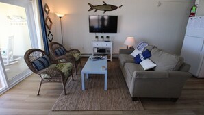A living room with wicker chairs, a grey sofa, a flat-screen TV, and a mounted fish decoration. - Calypso unit 701 located at 62nd street and Ocean front (Ocean City)